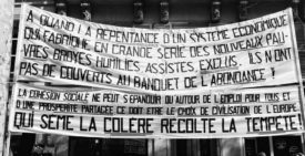 Black and white photo of two large banners with French text draped on a building. The top banner criticizes an economic system for creating poverty and exclusion; the bottom banner states that social cohesion requires shared prosperity. It was taken during a manifestation on 16 septembre 2010.