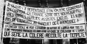 Black and white photo of two large banners with French text draped on a building. The top banner criticizes an economic system for creating poverty and exclusion; the bottom banner states that social cohesion requires shared prosperity. It was taken during a manifestation on 16 septembre 2010.