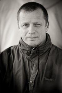 Black and white portrait of a man wearing a zippered Timberland jacket. With short hair and a neutral expression, he looks directly at the camera against a blurred background, reminiscent of the rugged marins from île d'Aix.