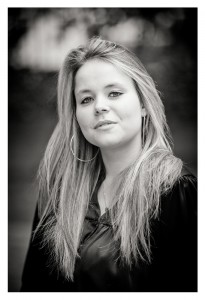 Black and white portrait of a young woman named Océane with long, straight hair, wearing hoop earrings and a dark top. She looks confidently at the camera with a slight smile, set against a blurred background.