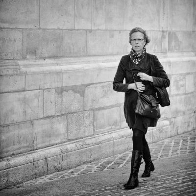 A Parisienne pressée marche sur un trottoir en briques.