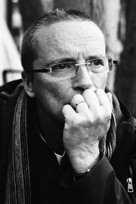 Songeur A man with short hair and glasses rests his chin on his fist, appearing deep in thought. He wears a striped scarf and a ring on his finger. The image is in black and white.
