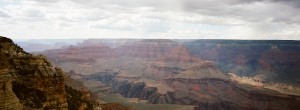 Image of the Grand Canyon with its expansive, layered rock formations stretching into the distance. The sky above is partly cloudy, casting soft shadows and light on the canyon's vast, rugged landscape. Captured in stunning detail by XPAN.