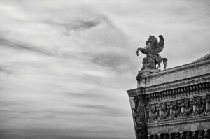 A black-and-white photo of the opéra Garnier’s ornate rooftop in Paris, featuring a dramatic statue of a winged horse and rider against a cloudy sky. The architectural details include sculpted faces and intricate designs on the toit.