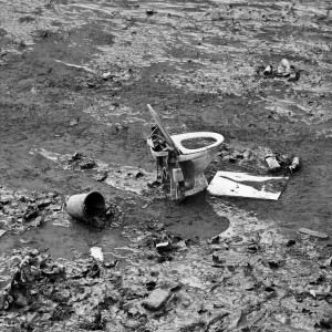A discarded toilet, a broken bucket, and scattered debris lie in a muddy, litter-strewn environment. The black and white image captures the scene of environmental neglect and pollution around Canal Saint-Martin after a vidange.