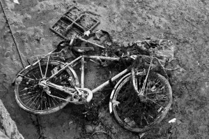 A black-and-white image depicts a heavily rusted, broken bicycle lying on the muddy ground by Canal Saint-Martin. The old bike is covered in mud and debris. Nearby, there's a metal grid and other encrusted items from the recent vidange, giving the scene an abandoned, decayed look.