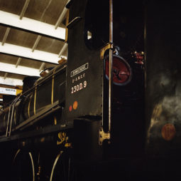 A close-up of a vintage black steam locomotive displayed indoors at Ground Control. The metal plate on the side reads "LEMBERGE" and "S.N.C.F. 230.D.9." Visible details include wheels, part of the tender, and a red valve. The roof and some additional exhibits from the Exposition are partially visible in the background.
