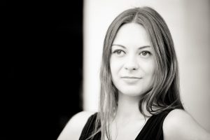 Anaïs, with long, straight hair and a slight smile, looks off-camera in this Noir et Blanc image. The blurred background highlights her face and upper body, evoking the timeless charm of Jardin du Palais-Royal.