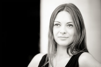 Anaïs, with long, straight hair and a slight smile, looks off-camera in this Noir et Blanc image. The blurred background highlights her face and upper body, evoking the timeless charm of Jardin du Palais-Royal.
