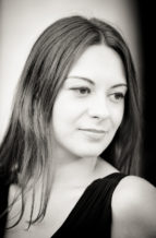 A Noir et Blanc portrait of Anaïs, a woman with long, straight hair, looking softly to the side in a calm expression. She is wearing a sleeveless, dark-colored top, evoking the timeless elegance of Jardin du Palais-Royal.