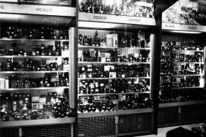 Black and white photo of glass display cases filled with cameras and equipment at Fotocasanova. Shelves are densely packed, with a sign above reading "ocasió," indicating this is a second-hand or used camera store.