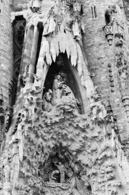 Detailed stone carvings adorn the façade of Barcelona’s iconic Sagrada Familia, featuring religious figures and intricate foliage patterns inspired by Antoni Gaudí. The ornate, dramatic architecture is beautifully captured in this black and white photo.