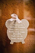 A sign shaped like a cartoon alarm clock displays business hours in Catalan, handwritten in white on a gray background with a white ribbon at the top, and is hung on a textured brown wall in Cambrils.