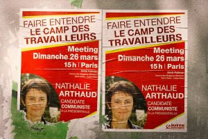 Two posters in French announce a political meeting featuring Nathalie Arthaud, a communist candidate. The event, part of her campaign, is scheduled for Sunday, March 26 at 3 PM in Paris. The posters are affixed to a green, worn surface and include a photo of Arthaud.