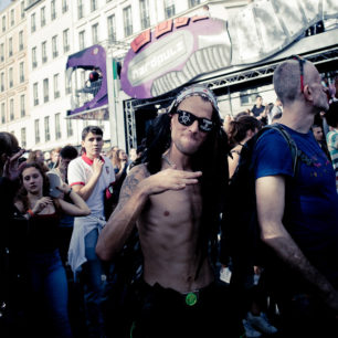 A topless man with long black hair, an eyepatch, and adorned with various accessories, poses with his hands up amidst the animated crowd at Techno Parade Edition 2017. A purple structure labeled "hardpulz" is visible in the background. People around appear engaged and energetic.