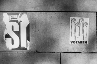 A black and white image showing two posters on a stone wall. The left poster features the word "SÍ" in large, bold text with a partial date above it, hinting at the Référendum de 2017 in Barcelone. The right poster shows four raised fists with the word "VOTAREM" below them, symbolizing the indépendance de la Catalogne.