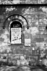 A wall with a gothic-style arched window is adorned with various posters and notes. The prominent poster in the window, referencing the "Référendum de 2017," reads "llibertat d'expressió" with illustrations and text below. Other smaller papers and signs about the indépendance de la Catalogne are attached to the wall around the window.