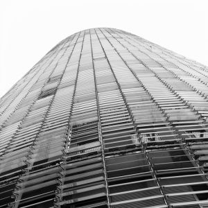 A low-angle view of a modern, high-rise building in Barcelone with a sleek, curved facade. The structure features horizontal lines and a grid-like pattern, reminiscent of the iconic tour Agbar, creating an impression of futuristic architecture against a stark white sky in Espagne.
