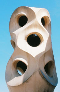 A close-up shot of a sculptural chimney on the roof of La Pedrera (Casa Milà), a famous building in Barcelona designed by Antoni Gaudí. Titled "Sans titre," the structure features organic, swirl-like shapes with multiple circular openings, set against a clear blue sky.