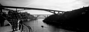 A black-and-white panoramic photo, titled "Sans Titre," captures two bridges spanning across a river. Positioned one above the other, a boat glides along the water. The hills on both riverbanks are adorned with buildings, all under a cloudy sky.