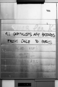 A metal surface with graffiti that reads "ALL CAPITALISTS ARE BASTARDS FROM CHILE TO PARIS," marked during the manifestation on 11 Janvier 2020. Additional tags like "ACAB FDP!", "Macron FDP," and other partially visible inscriptions are written in black marker on a silver-colored backdrop, protesting the réforme des retraites.