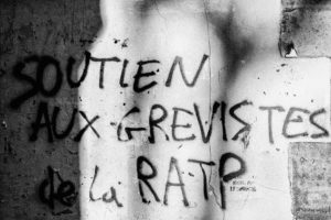 A black-and-white photo of graffiti on a wall that reads: "SOUTIEN AUX GREVISTES de la RATP," translating to "Support for the strikers of the RATP" in French. The bold, uppercase message was likely inspired by the manifestation against réforme des retraites on 11 janvier 2020, conveying firm solidarity.