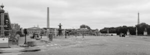 A black and white image of Place de la Concorde in Paris. The scene shows an obelisk at the center, surrounded by construction scaffolding. In the background, you can see parts of the Eiffel Tower and other historic buildings. The area appears quiet and empty.