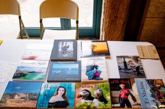 A table showcasing an array of photography books and magazines, each adorned with unique covers featuring landscapes, animals, and people. Two white chairs are positioned in the background near a window, reminiscent of a cozy corner at Expo Photos Onzain.
