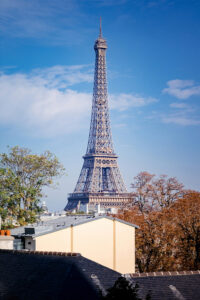 The Eiffel Tower rises above trees and rooftops under a blue sky with scattered clouds in Paris, France.