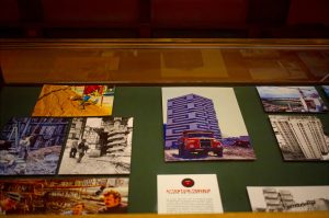 Photographs of construction scenes and buildings from Paris, 1970 are displayed in a glass case, including images of workers, machinery, and a red lorry in front of a modern patterned building.