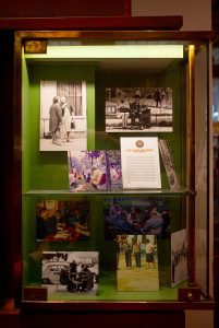 A glass display case with vintage black-and-white and colour photos of people socialising at Parisian cafés in the 1970s, plus an informational card titled "Les Cafés de Paris.