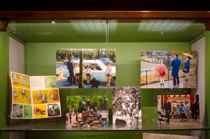 A display case with vintage photos of families and children, a park scene in 1970s Paris, a playground, and an open illustrated book with drawings of children and furniture.