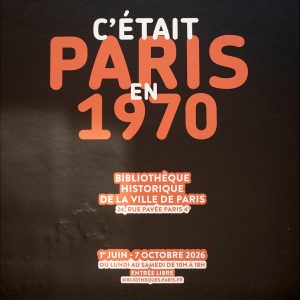 Text on a black wall reads: “C’était Paris en 1970. Bibliothèque Historique de la Ville de Paris. 1er juin–7 octobre 2026. Entrée libre.” This striking display evokes the spirit of Paris in 1970, inviting visitors to explore the city’s rich history.