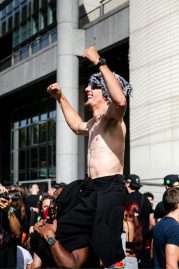 20260919-5H1A0227_MOD_FRAME_resize A bare-chested man with sunglasses and a hat raises his arms in excitement whilst sitting on another person’s shoulders at a crowded outdoor event during the 2026 Paris Techno Parade.
