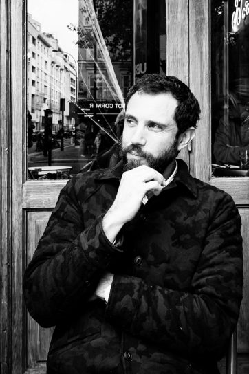 Jean Benoit Roubinet sits by a window, looking off to the side with his hand to his chin.