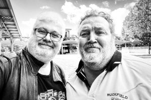 Two middle-aged men with white beards stand side-by-side for a selfie outdoors at the Salon de la photo in Paris.