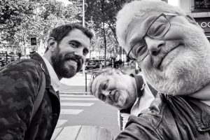 Three men posing for a close-up selfie on a Paris city street during the Salon de la photo.