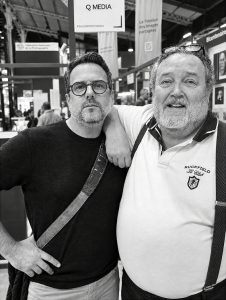 Two middle-aged men, including Jean Benoit Roubinet, posing for a photo with one man resting his arm on the other’s shoulder at the Salon de la Photo 2026.