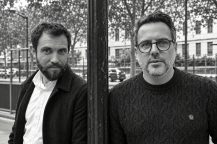 Two men standing on either side of a dark metal post at the Salon de la photo.