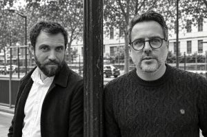 Two men standing on either side of a dark metal post at the Salon de la photo.
