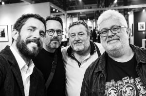 Four men smile together for a group photo with Jean Benoit Roubinet in a Salon de la photo gallery space.
